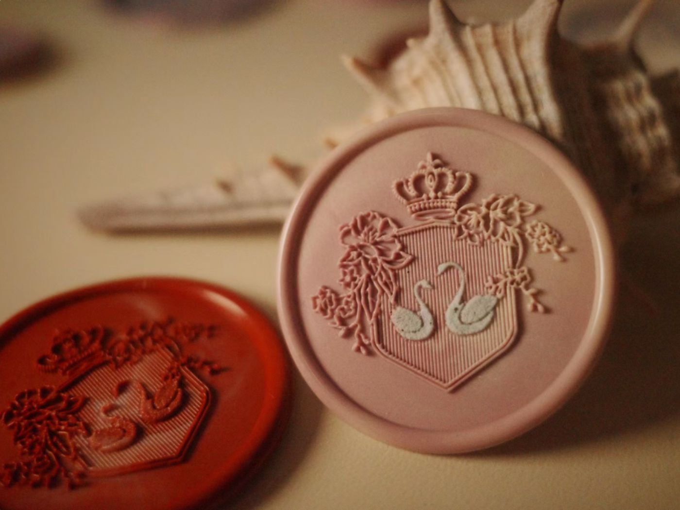 Elegant wax seals featuring swan designs in pink and red, with crown and floral details embossed on circular stamps