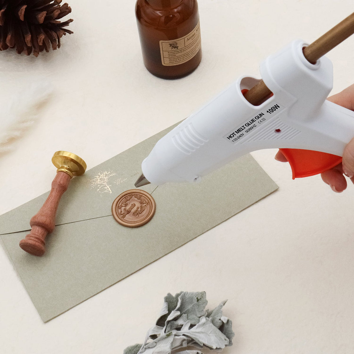 Electric hot melt glue gun sealing wax on envelope with wooden wax seal stamp and amber bottle background